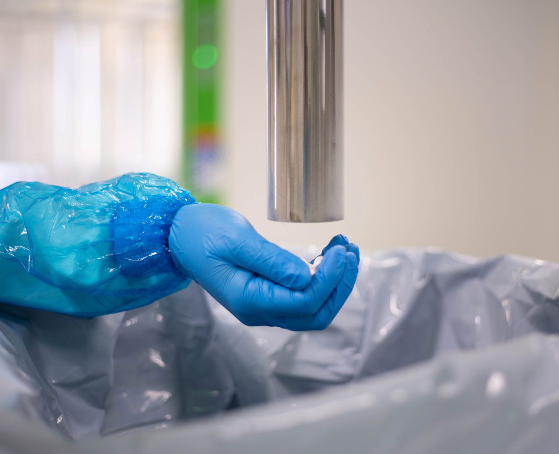 Main gantée avec manchette de protection tendue sous un objet cylindrique métallique dans un environnement de laboratoire.