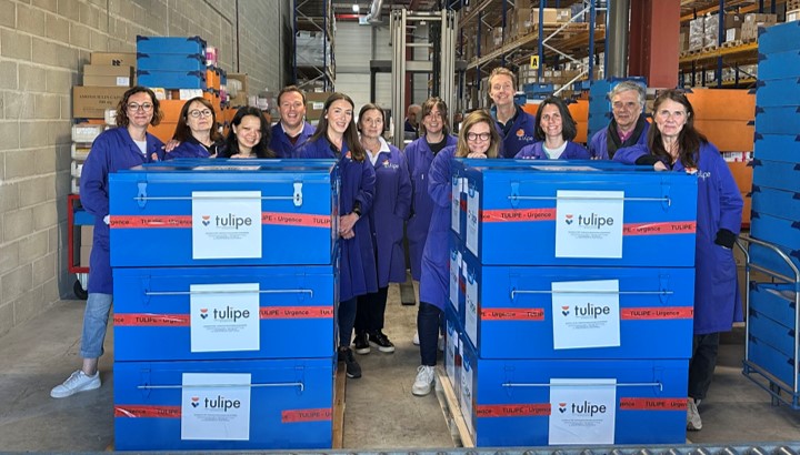 Photo de groupe de plusieurs collaborateurs Viatris dans l'entrepôt de l'Association Tulipe, derrière des kits de produits de santé