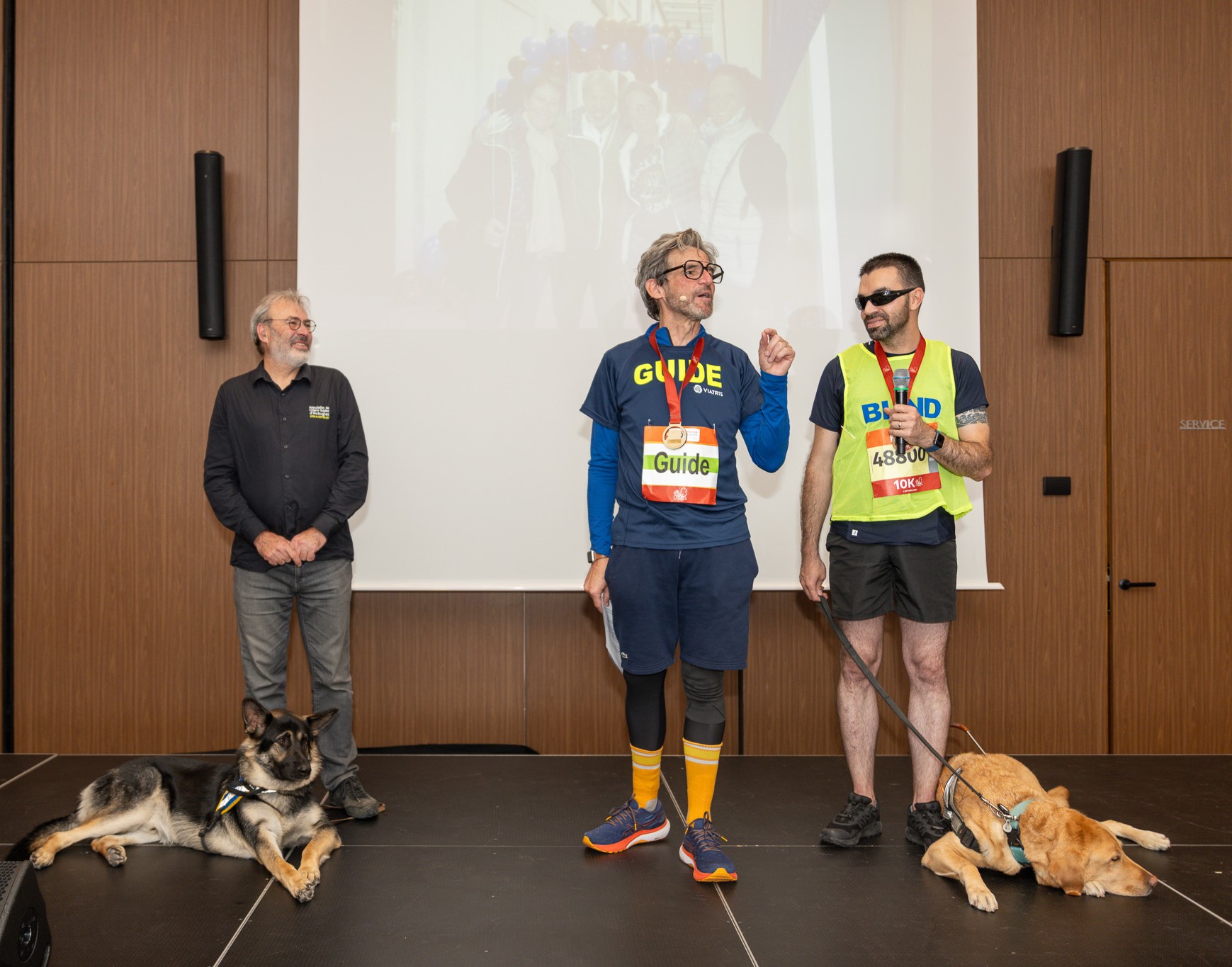 Roland Donzelle, Christophe Maupas et Pierre-Marie Micheli sur une scène avec deux chiens guides.