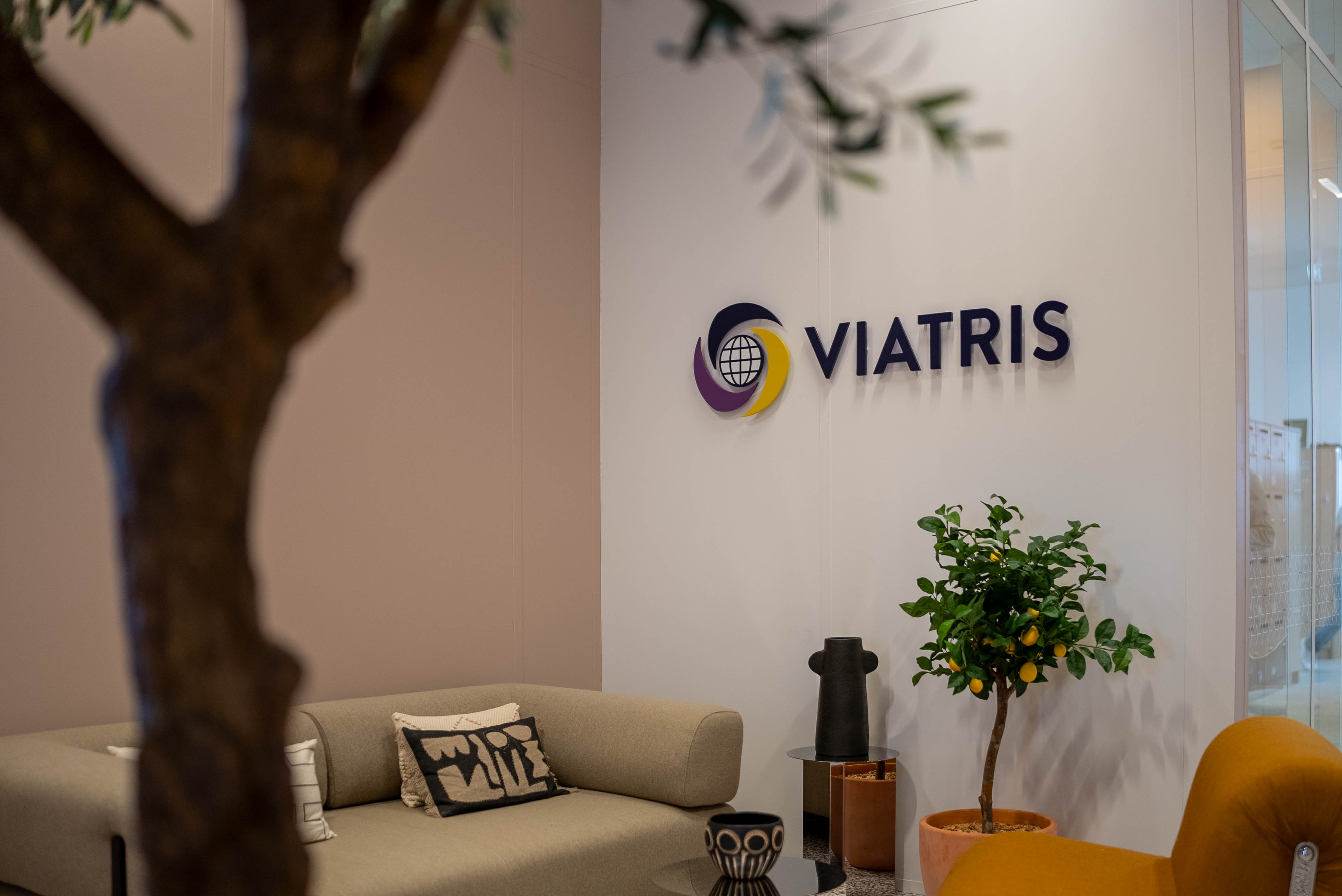 Intérieur des bureaux de Viatris à Paris, avec le logo Viatris sur un mur, au-dessus d'un canape, de plantes et d'objets décoratifs.