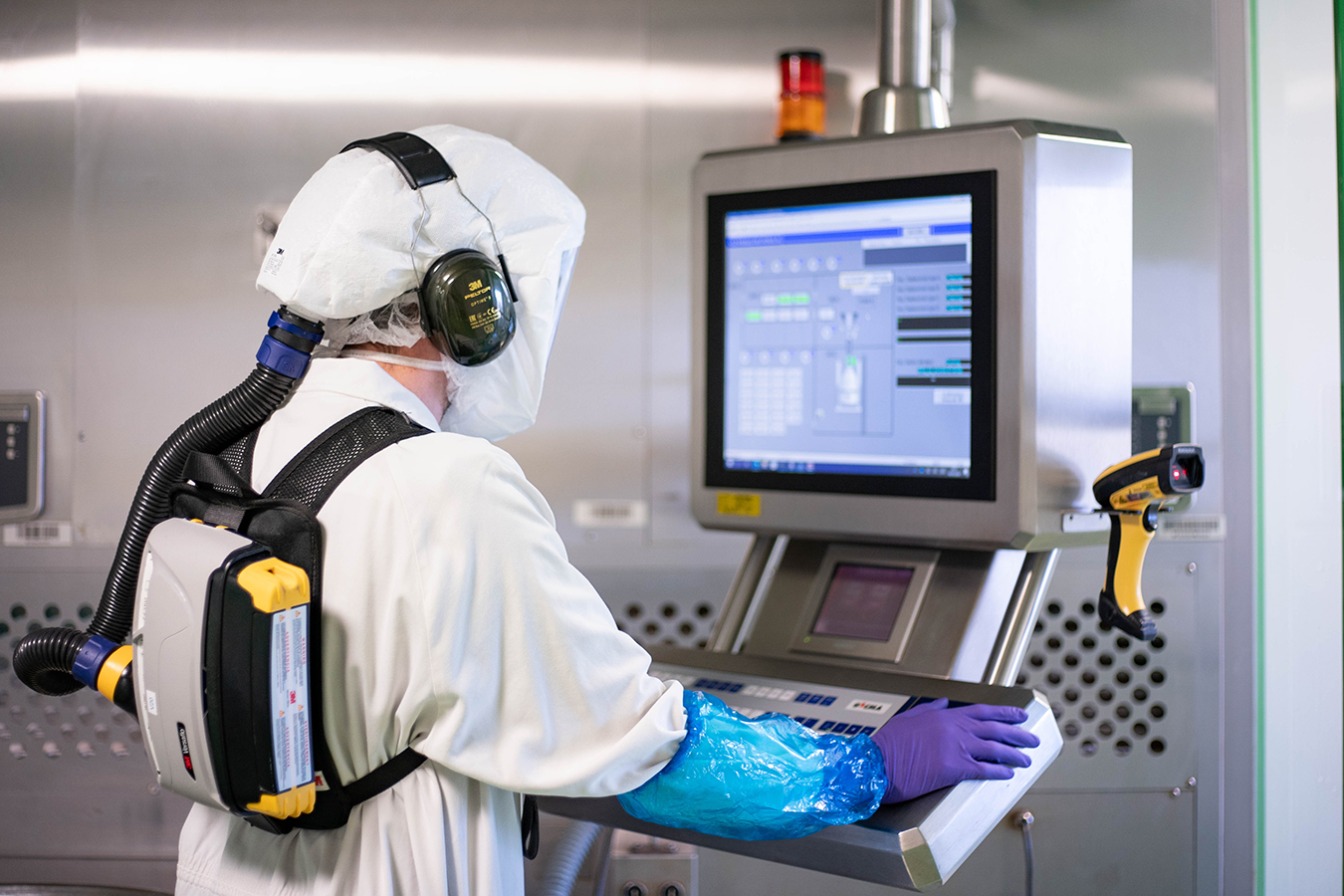 Collaborateur Viatris en blouse blanche et équipement de protection contrôlant une machine sur un écran en salle de production pharmaceutique