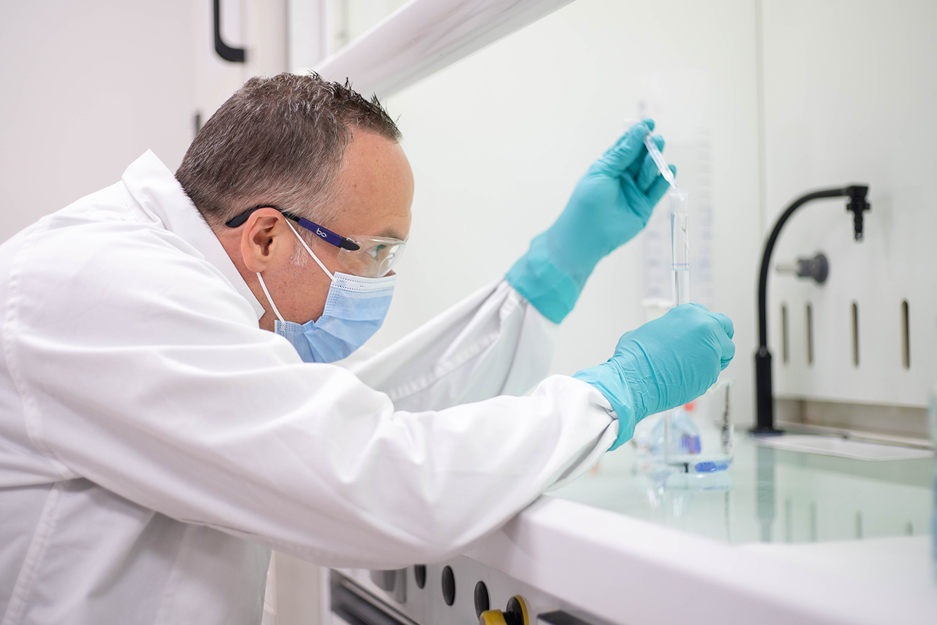 Scientifique Viatris en blouse blanche, masque et gants manipulant un échantillon liquide en laboratoire pharmaceutique