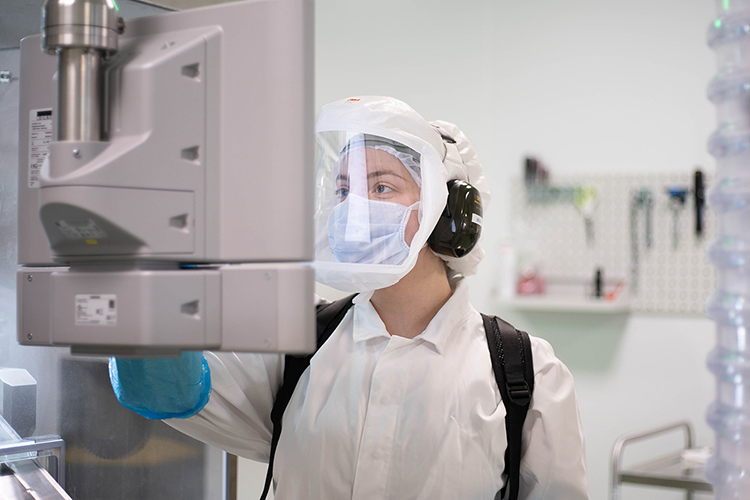 Collaboratrice Viatris en blouse blanche et équipements de protection inspectant une machine en laboratoire pharmaceutique